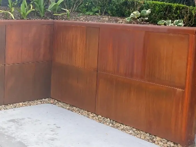 Hand tools resting against a partially installed steel retaining wall.